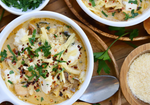 Bowl of cheesy white lasagna soup with Springer Mountain Farms chicken, topped with melted cheese, fresh parsley, and red pepper flakes, served with Parmesan and toasted bread.