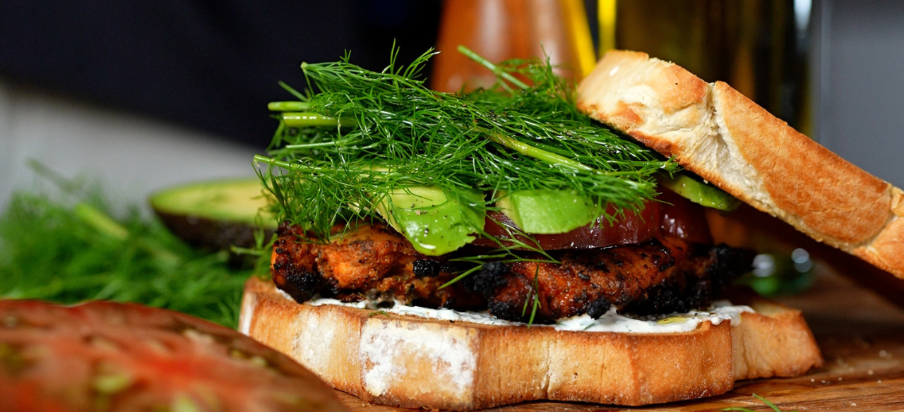 Grilled chicken bacon ranch sandwich stacked with juicy chicken breast, crispy bacon, avocado, fresh dill, heirloom tomato, and creamy ranch dressing on toasted white bread.