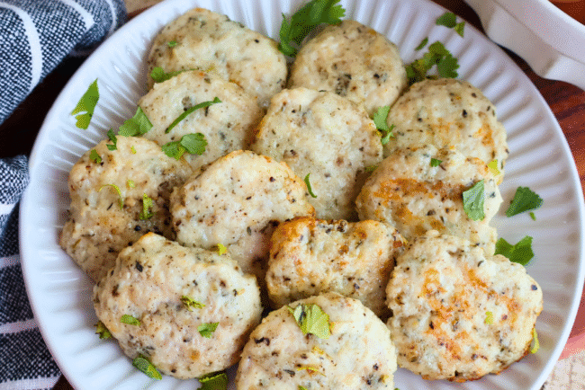 Homemade chicken breakfast sausage patties on a white plate, garnished with fresh parsley. Juicy, golden-brown, and perfectly seasoned, these protein-packed chicken sausages make a healthy, flavorful breakfast option made with Springer Mountain Farms Simply Superior Chicken™.