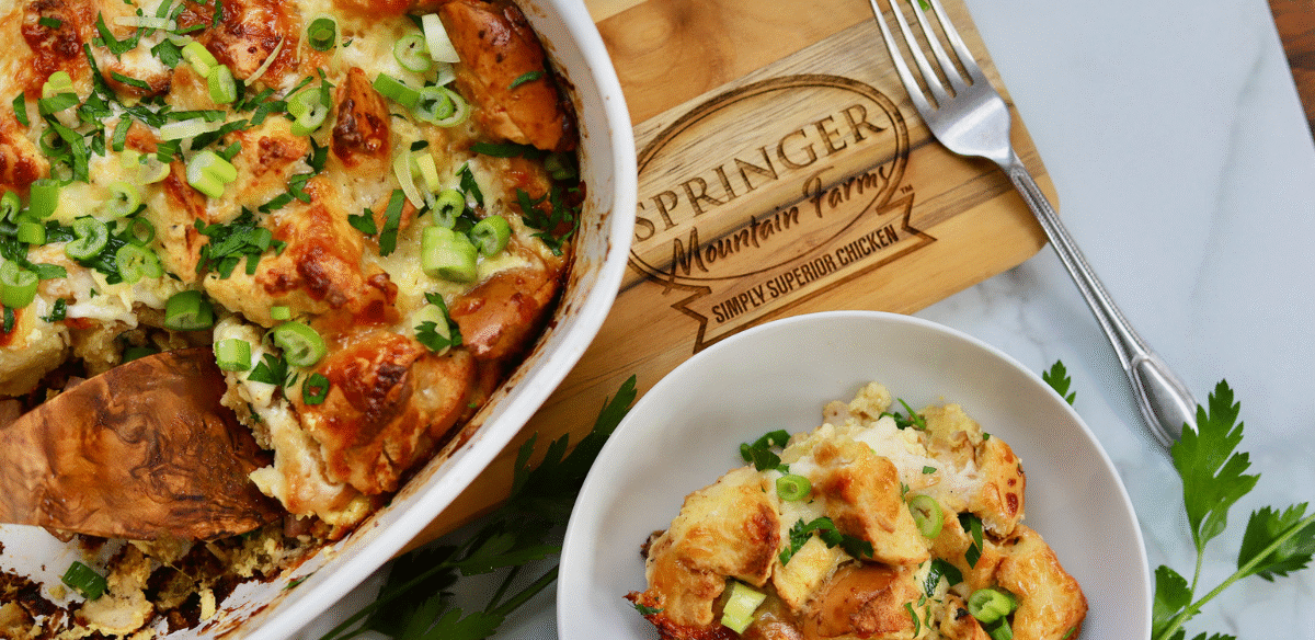 Golden baked chicken cordon bleu casserole topped with toasty bagel pieces, melted cheese, and fresh green onions, served in a dish with a side portion.