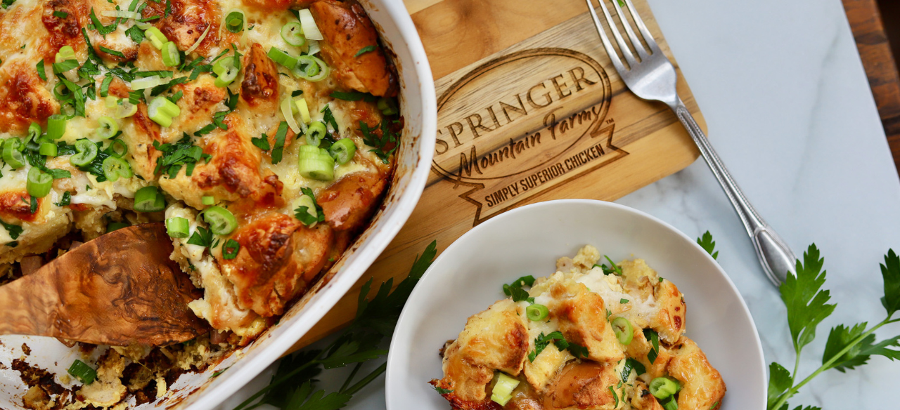 Golden baked chicken cordon bleu casserole topped with toasty bagel pieces, melted cheese, and fresh green onions, served in a dish with a side portion.