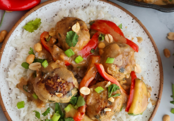 Ground chicken meatballs in creamy peanut sauce served over white rice with red bell peppers, green onions, and peanuts.