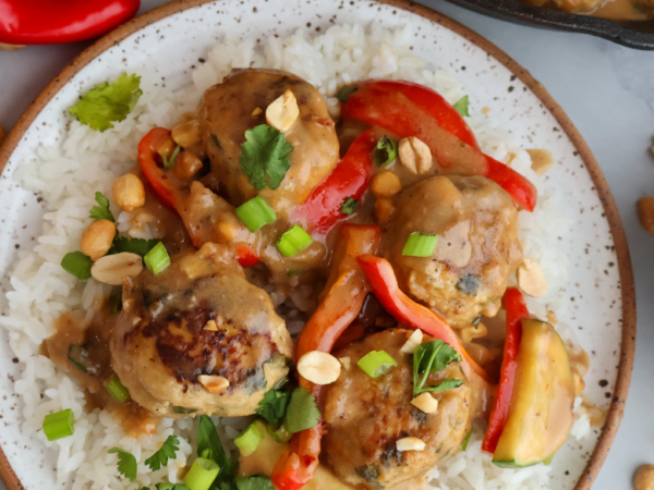 Ground chicken meatballs in creamy peanut sauce served over white rice with red bell peppers, green onions, and peanuts.