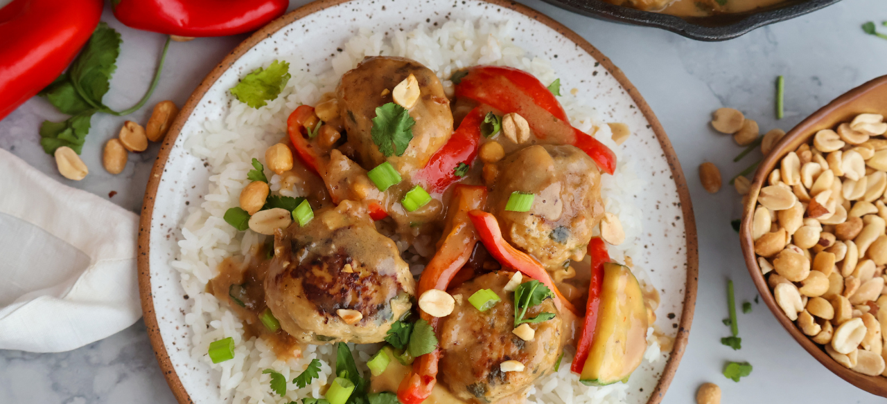 Ground chicken meatballs in creamy peanut sauce served over white rice with red bell peppers, green onions, and peanuts.
