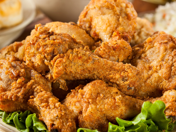 Classic Southern fried chicken drumsticks piled high on a platter with fresh lettuce, served alongside coleslaw, biscuits, and macaroni and cheese.