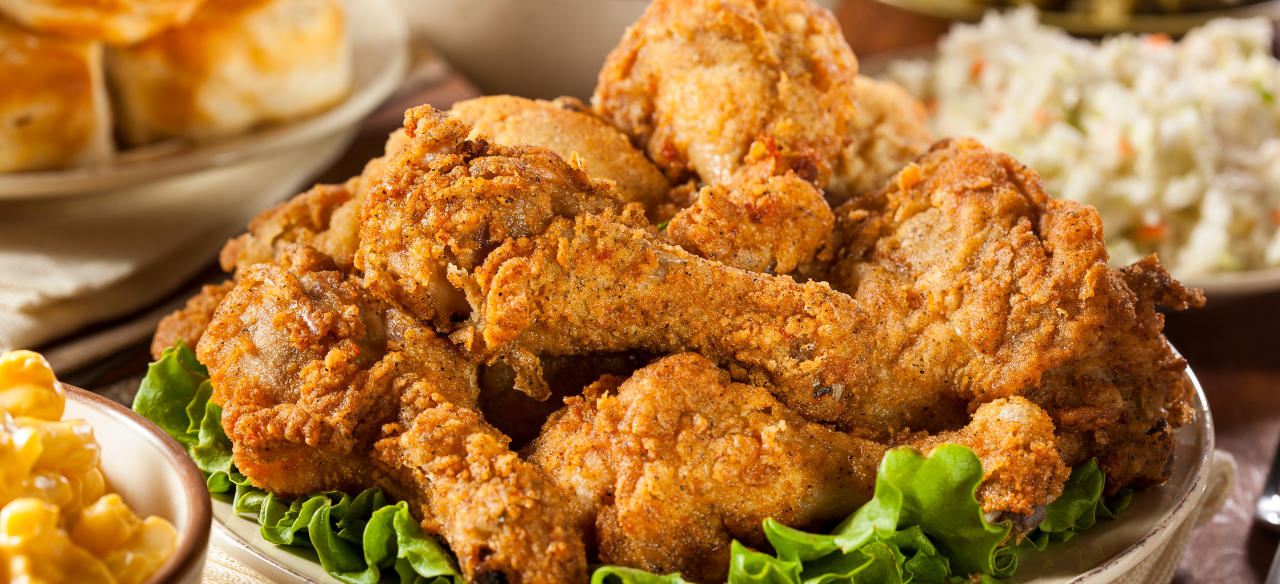 Classic Southern fried chicken drumsticks piled high on a platter with fresh lettuce, served alongside coleslaw, biscuits, and macaroni and cheese.