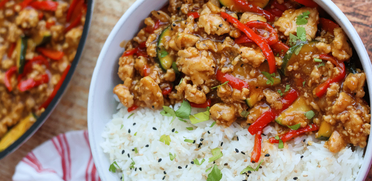 Savory ground chicken stir fry with red bell peppers, zucchini, and a flavorful sauce served over fluffy white rice with sesame seeds and fresh herbs.