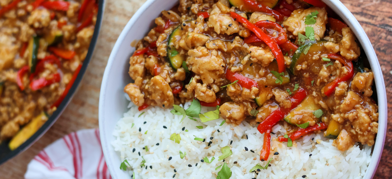 Savory ground chicken stir fry with red bell peppers, zucchini, and a flavorful sauce served over fluffy white rice with sesame seeds and fresh herbs.