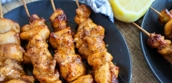 Grilled lemon butter chicken skewers on a black plate with lemon wedges – easy chicken kabobs for summer grilling
