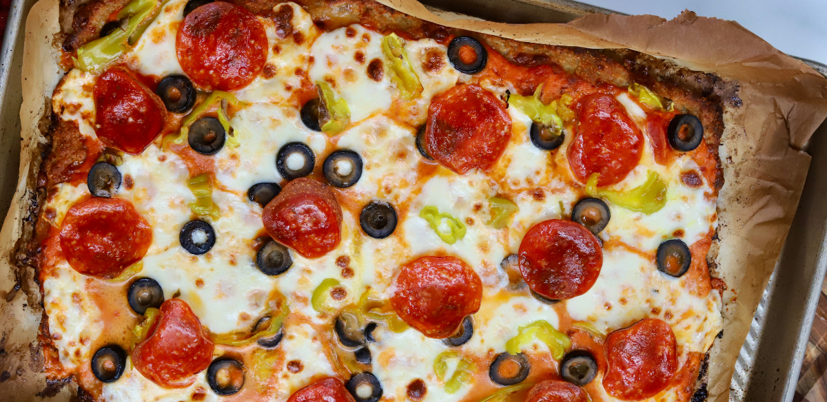 High-protein pizza made with a ground chicken crust, topped with melted mozzarella, pepperoni, black olives, banana peppers, and marinara sauce.