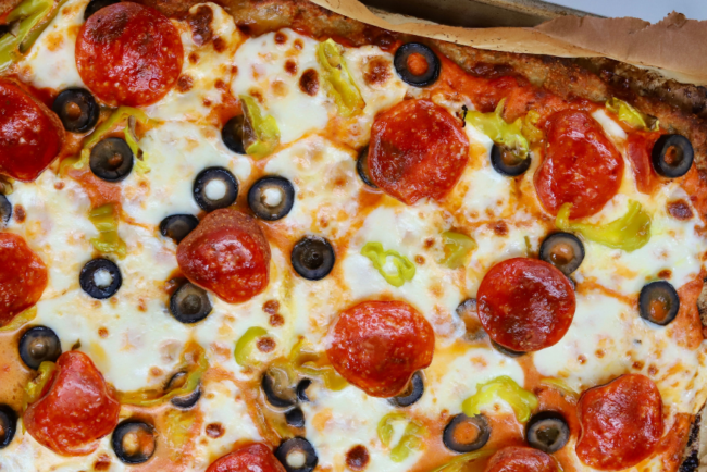 High-protein pizza made with a ground chicken crust, topped with melted mozzarella, pepperoni, black olives, banana peppers, and marinara sauce.