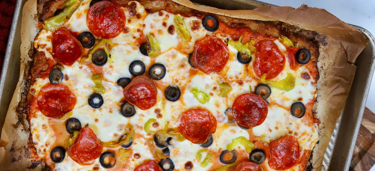 High-protein pizza made with a ground chicken crust, topped with melted mozzarella, pepperoni, black olives, banana peppers, and marinara sauce.