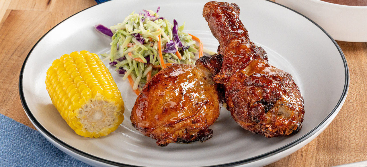 Air fryer chicken drumsticks glazed with peach BBQ sauce served with coleslaw and corn on the cob