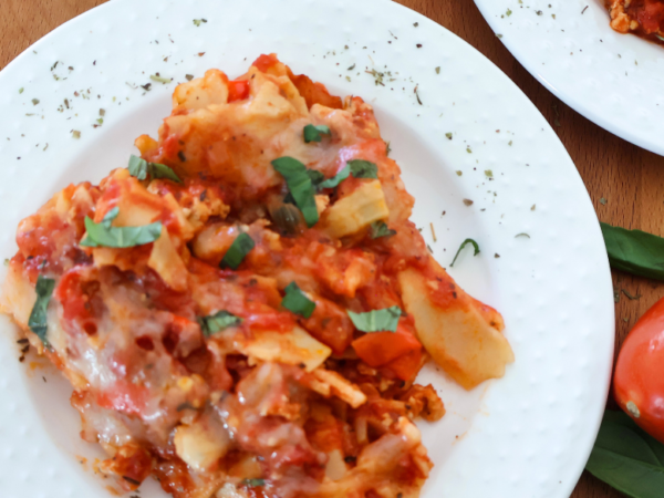 Lazy lasagna made with ground chicken, lasagna noodles, tomato sauce, and melted mozzarella topped with fresh basil on a white plate.