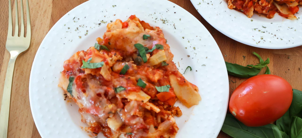 Lazy lasagna made with ground chicken, lasagna noodles, tomato sauce, and melted mozzarella topped with fresh basil on a white plate.