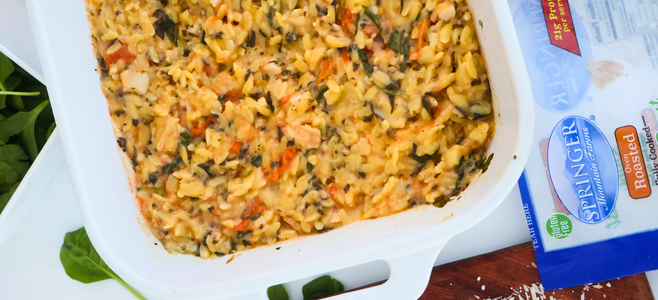 One pan spinach artichoke chicken orzo bake in a white casserole dish with roasted chicken, tomatoes, and spinach