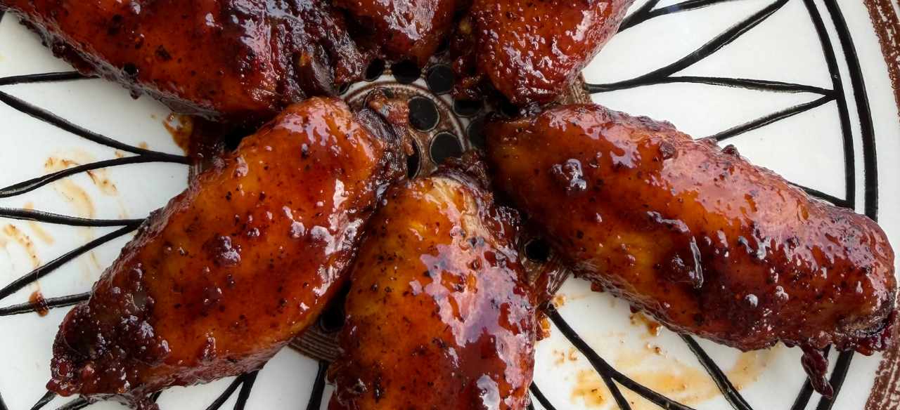 Close-up of smoky barbecue chicken wings coated in a thick, glossy BBQ sauce, arranged on a decorative plate with a rich caramelized finish and charred edges.